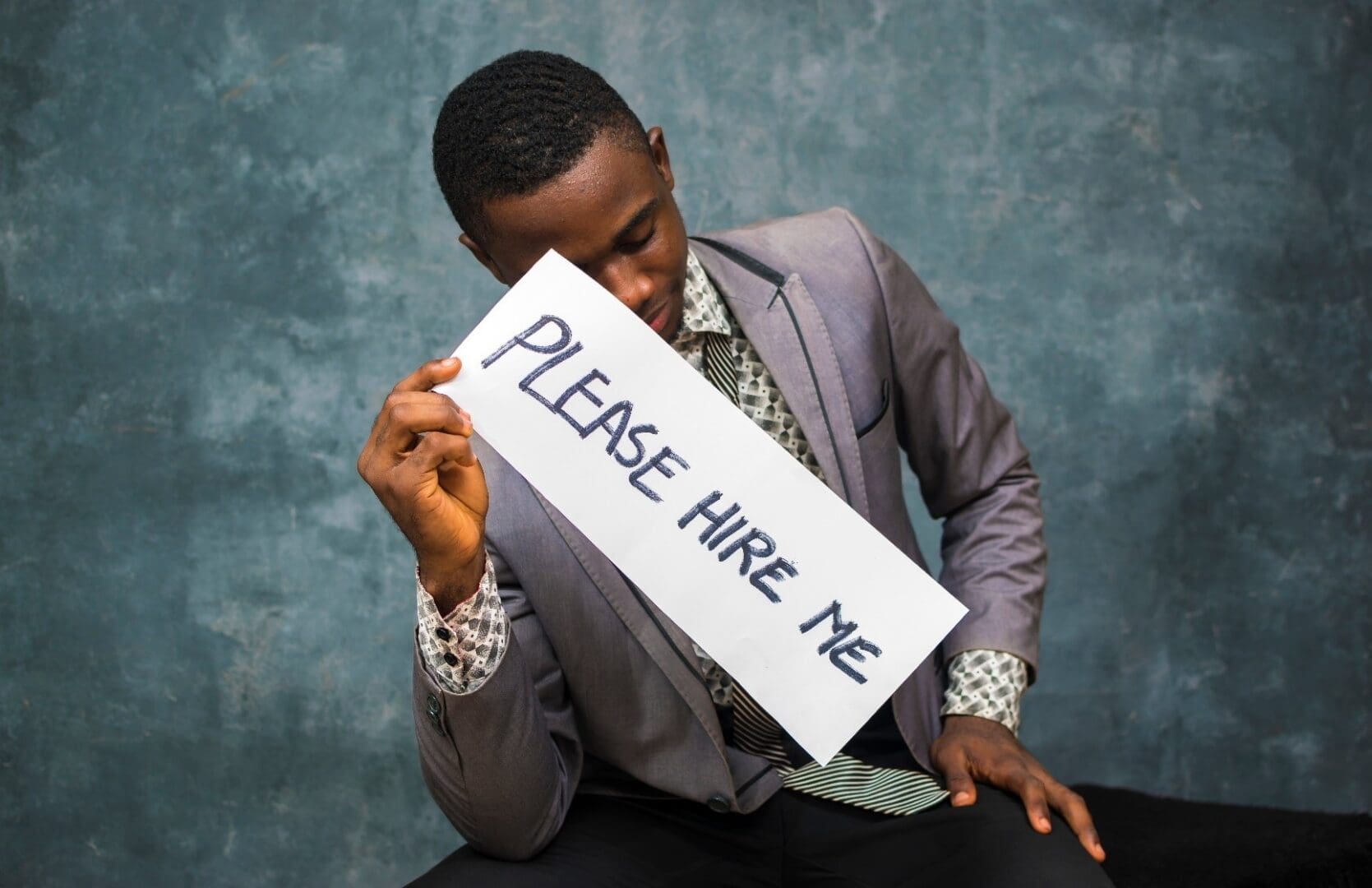 A man holding a sign that says please hire me.