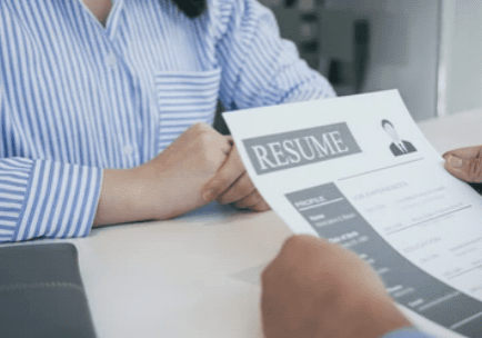 A person is holding a resume in front of a desk.
